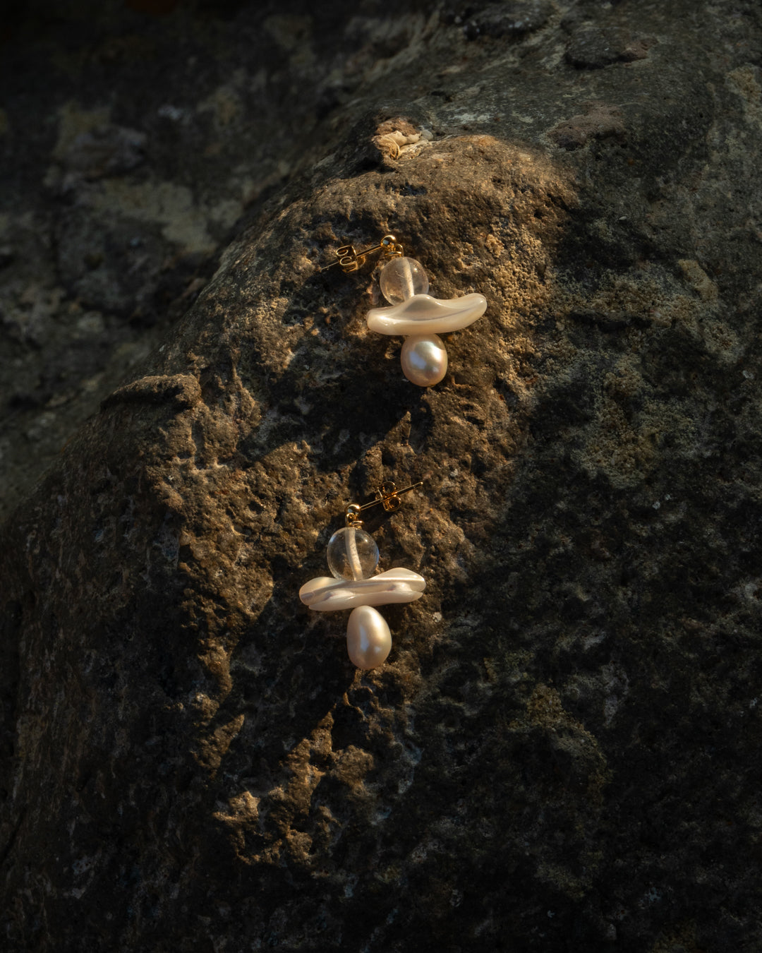 Clear quartz and freshwater pearl Echo Earrings, each featuring a beautiful combination of natural materials and exquisite craftsmanship, set against a rustic rock backdrop, highlighted by the last ray of sunlight before dusk.