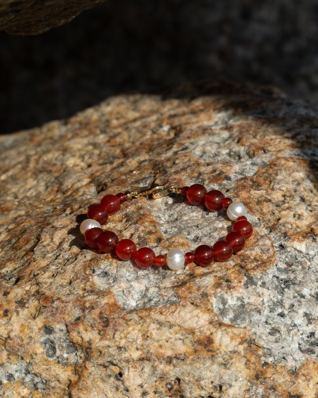 Eterna Nova Bracelet, red agate and freshwater pearl, handcrafted and set against rocky backdrop.
