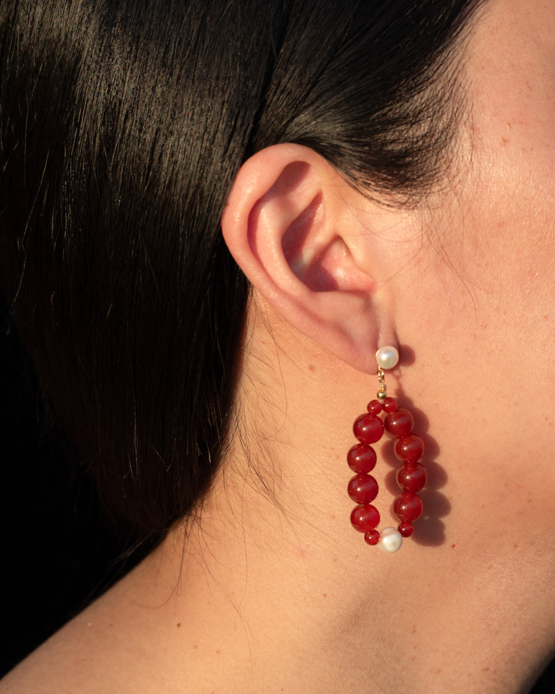 Freshwater pearl and red agate Eterna Nova earrings, elegantly worn in a close-up portrait.