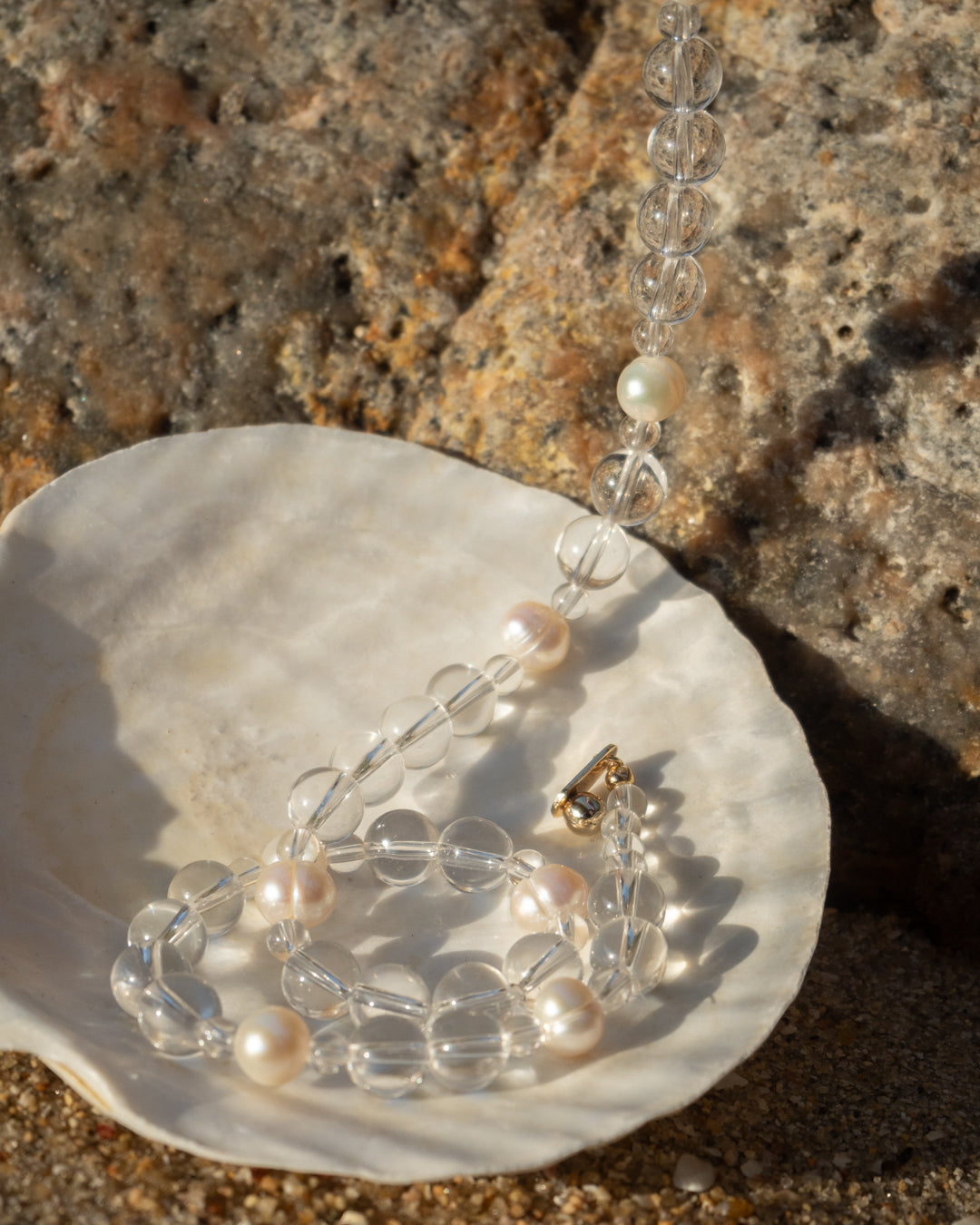 Jewelry set with clear quartz and freshwater pearl, showcasing the delicate beauty of Eterna Nova necklace's materials and intricate design, displayed on a seashell.