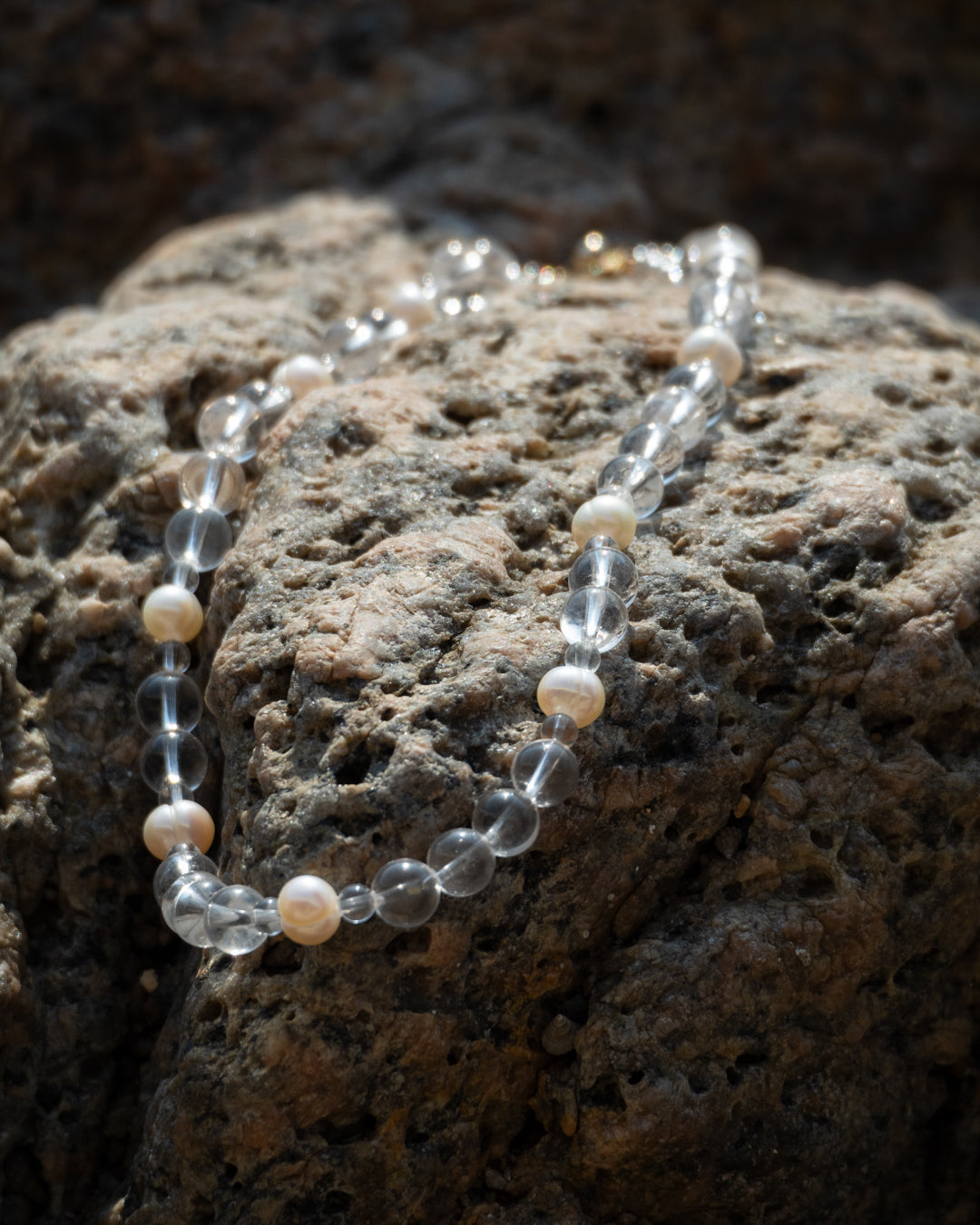 Eterna Nova necklace, featuring clear quartz beads and a freshwater pearl, elegantly displayed on rock formation.