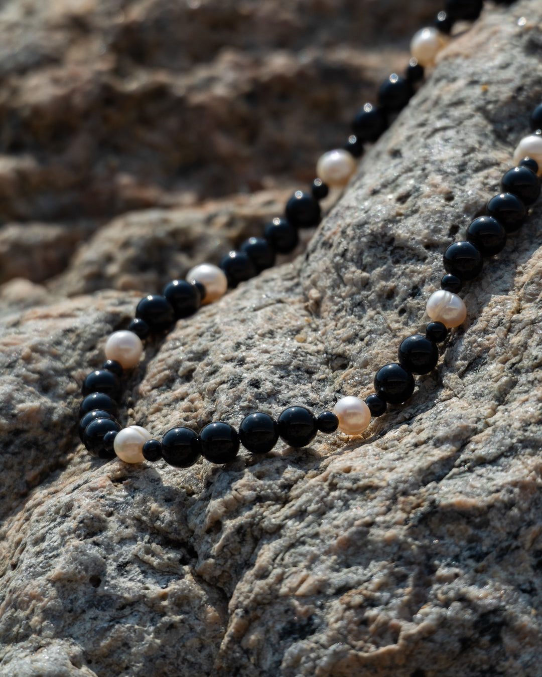 Eterna Nova necklace, A black onyx necklace featuring a freshwater pearls, captured against a rock backdrop.
