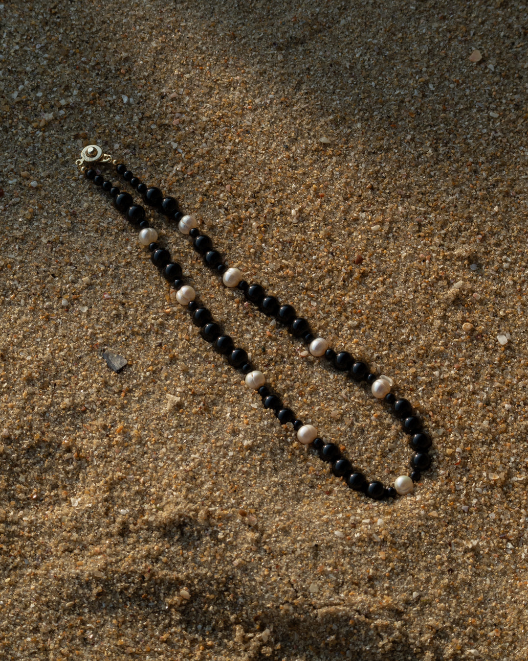 Elegant Eterna Nova Necklace featuring freshwater pearls and onyx beads, captured in a serene beach setting.