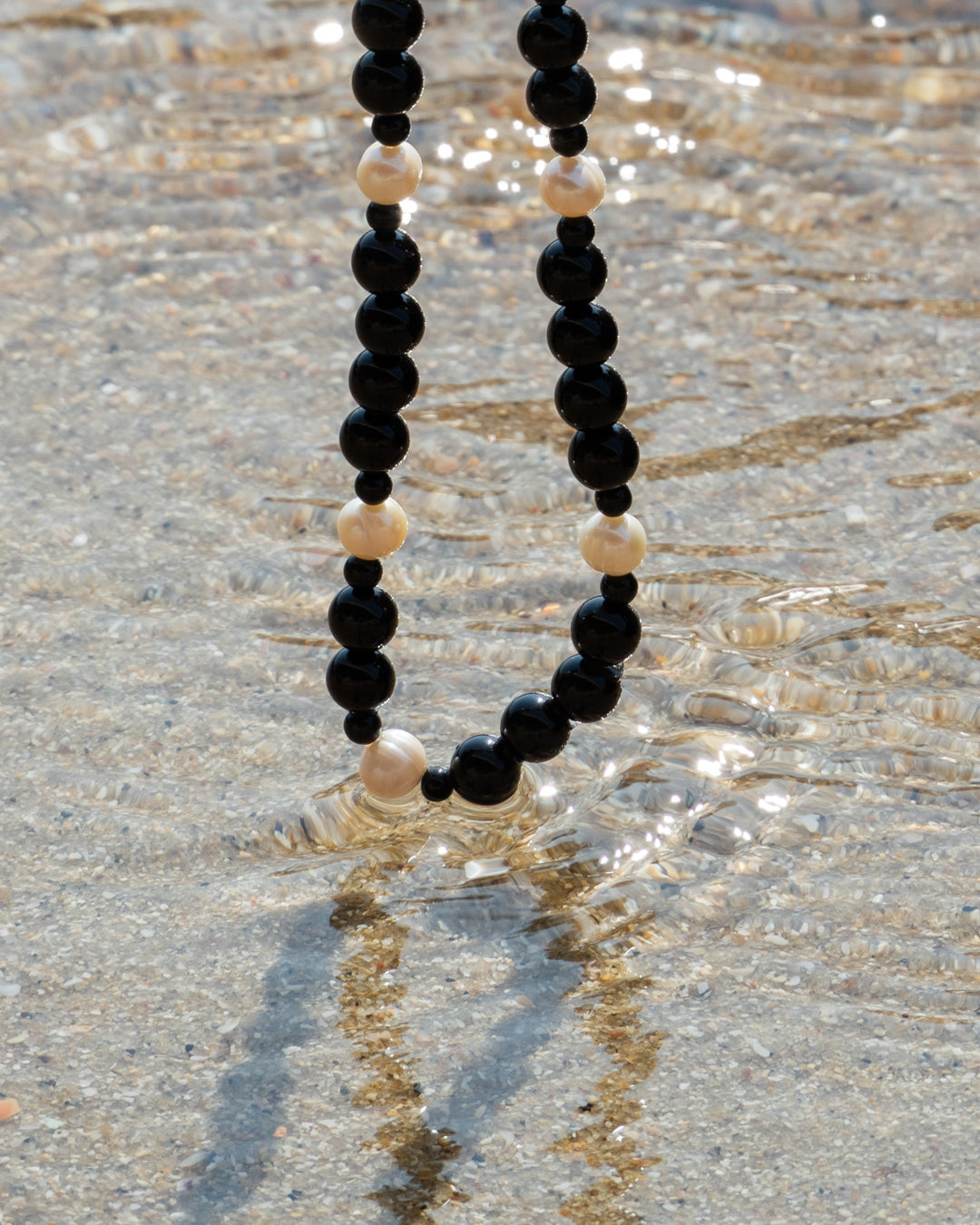 Freshwater pearl and onyx Eterna Nova Necklace resting on a wet beach, ready for a serene seaside adventure.