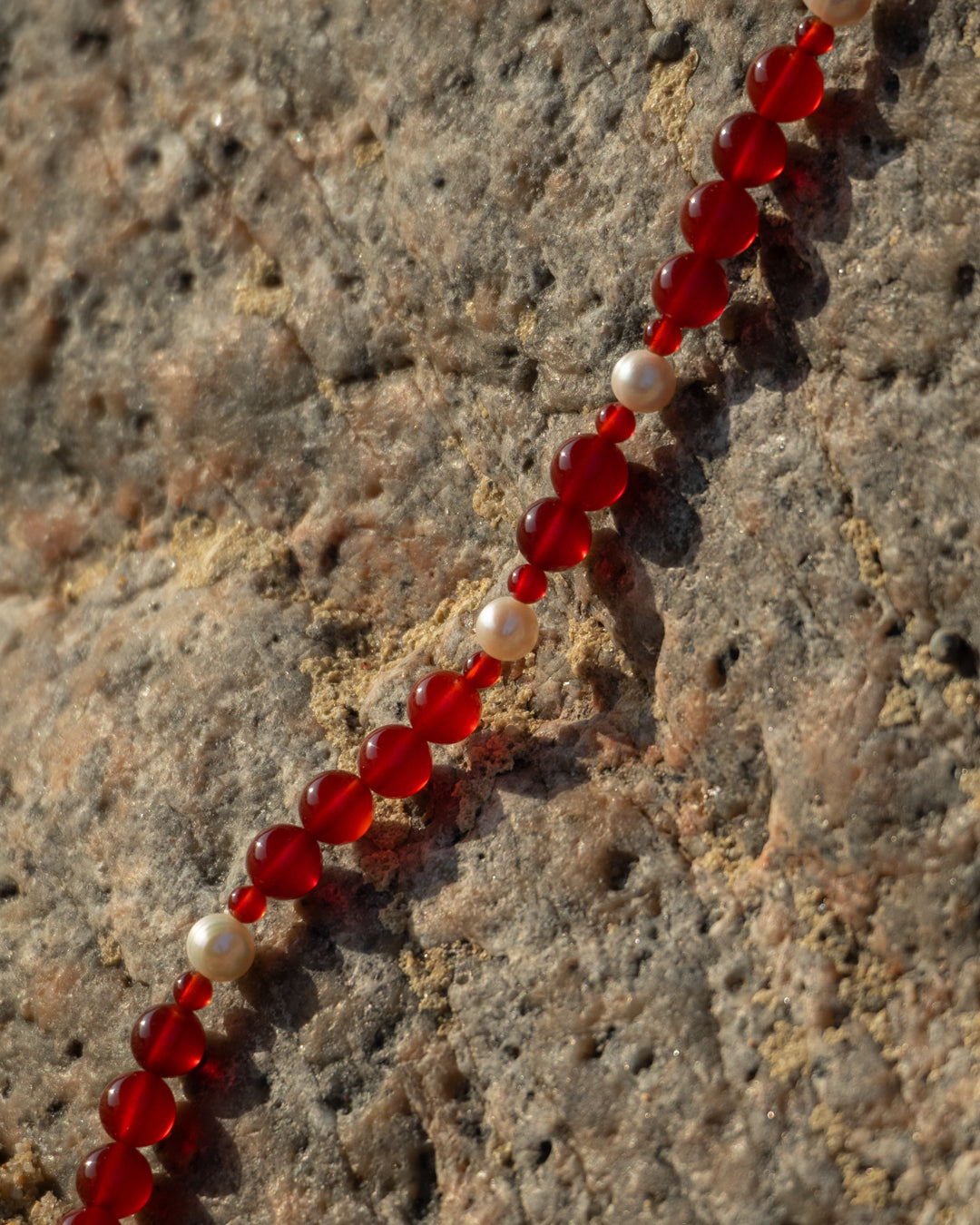 Red Eterna Nova Necklace with Freshwater Pearls, set against a rocky backdrop.