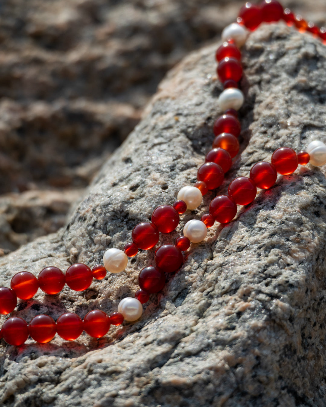 Eterna Nova Necklace: Red Agate and Freshwater Pearl Jewelry featuring red agate beads on a freshwater pearl necklace, placed on a rocky surface.