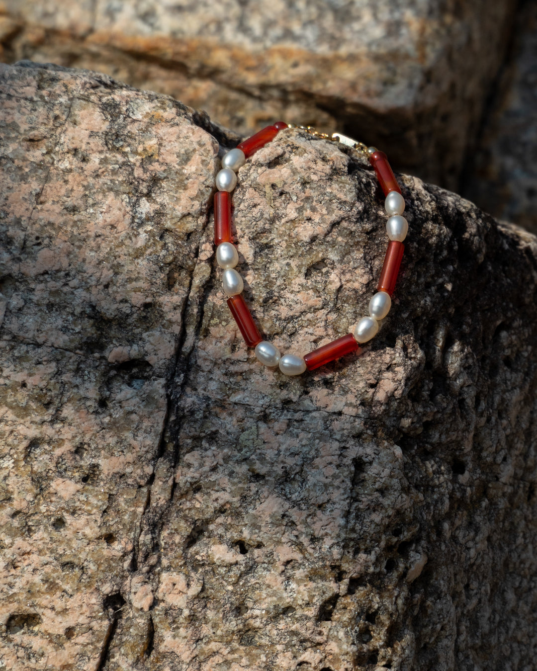 Rhythm bracelet: red agate and freshwater pearl, a chic accessory showcasing natural beauty, crafted for everyday elegance on a rocky surface.