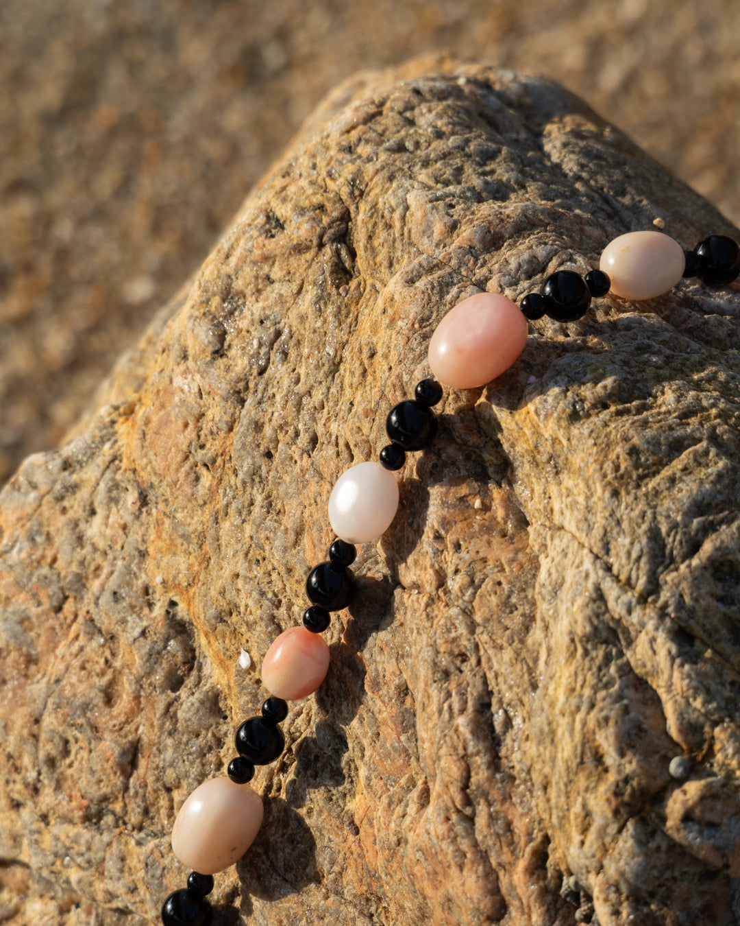 Pink opal and onyx Sonata Blush necklace, elegantly laid out against a rock background for showcasing its natural stone charms.