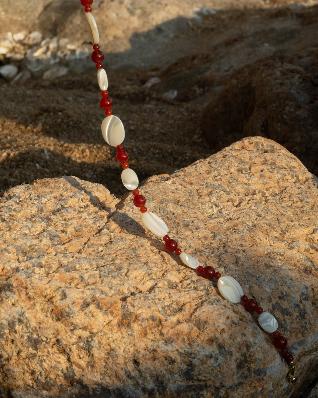 Red and silver Sonata Moonlit Necklace, featuring mother of pearl beads and red agate gemstones on a rocky beach background.