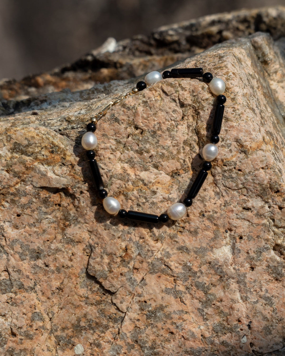 Starry Bracelet onyx: Black onyx and freshwater pearl bracelet, elegantly displaying its vibrant materials against a contrasting stone wall background, serving as a sophisticated accessory for everyday wear.