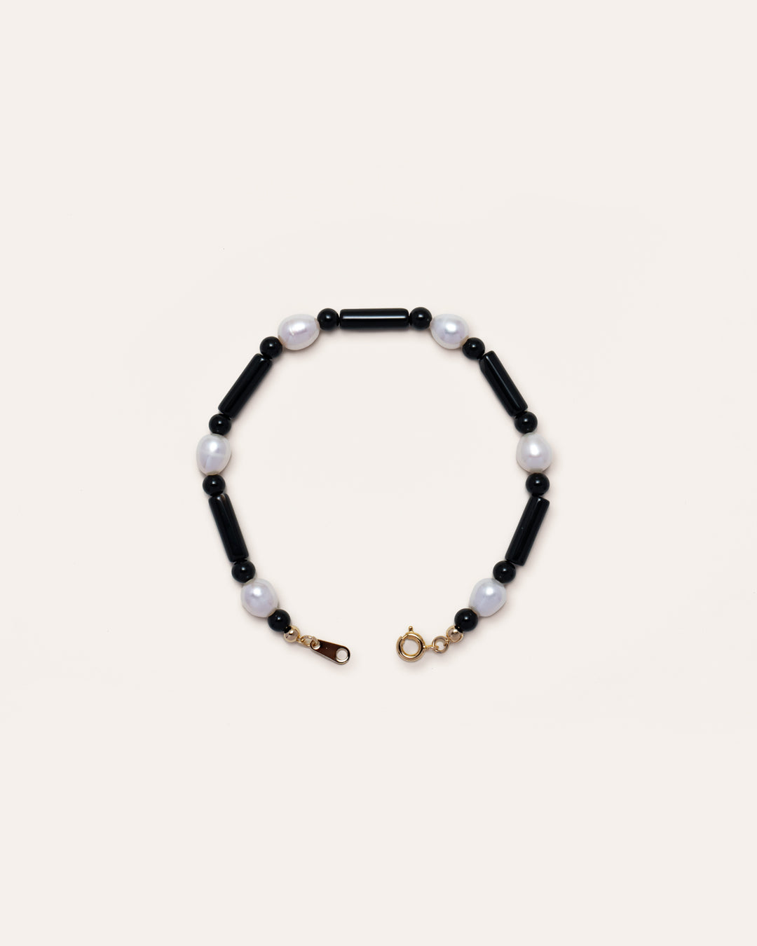 Starry Bracelet: A delicate black bracelet with onyx and freshwater pearl beads, featuring a gold clasp, presented against a minimalist grey background.