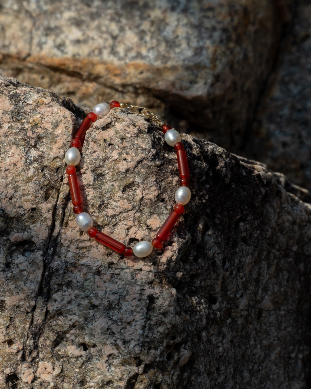 Starry Bracelet Red Agate, A handcrafted bracelet featuring red agate gemstones and a freshwater pearl, set against a rocky background.