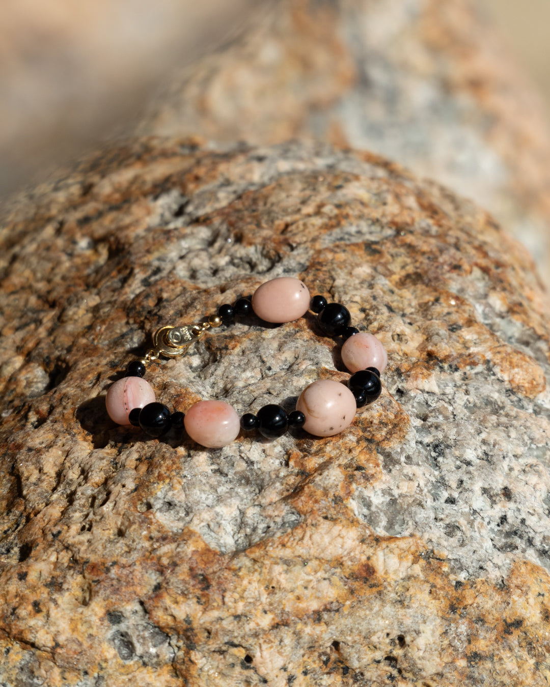 Pink opal and onyx Sonata Blush bracelet against a rock background. Elegant jewelry with a delicate blend of pink and black stones, perfect for everyday wear or as a gift.