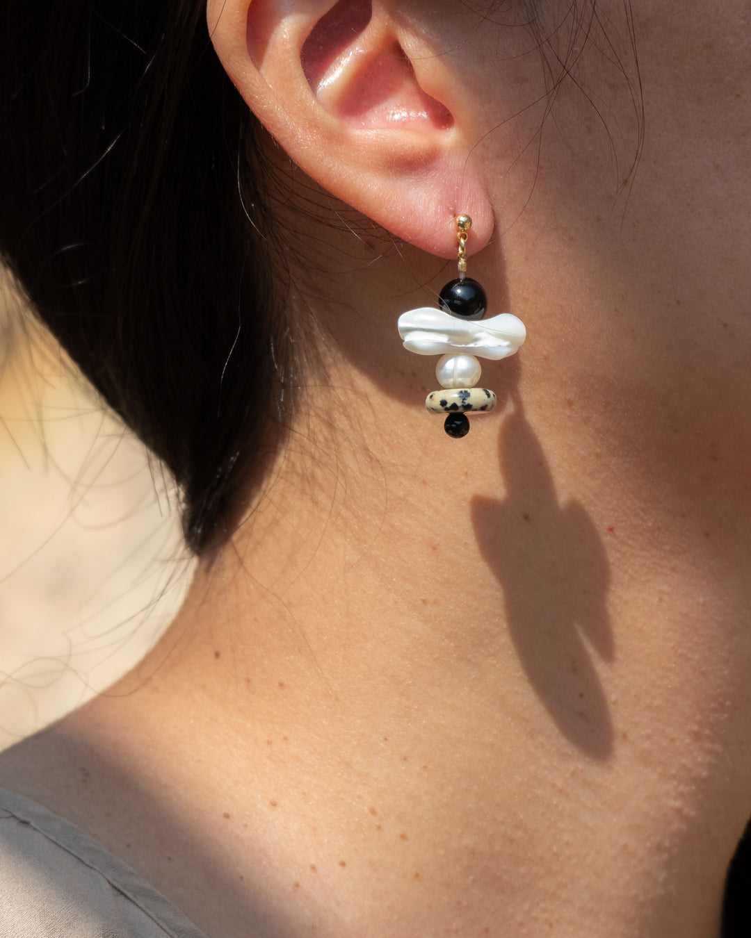 Tulip Earrings: Chic earrings, delicate fusion of mother of pearl and freshwater pearls, onyx and dalmatian jasper, worn by a model, exude elegance.