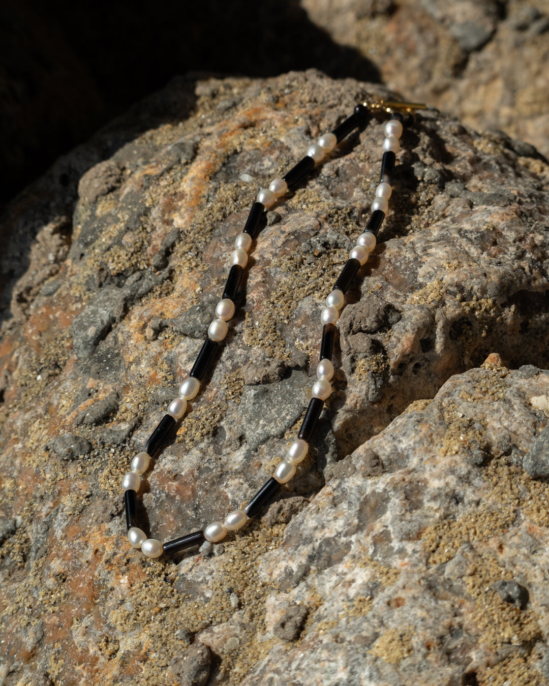 Rhythm Necklace - Freshwater Pearl and Onyx: A stunning statement piece made from lustrous freshwater pearls and contrasting onyx stones, displayed on a rock background.