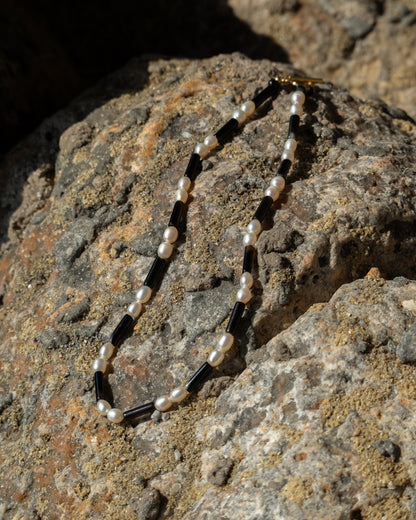 Rhythm Necklace - Freshwater Pearl and Onyx: A stunning statement piece made from lustrous freshwater pearls and contrasting onyx stones, displayed on a rock background.