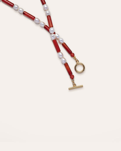 Rhythm Necklace, a sleek necklace featuring freshwater pearls and vibrant red agate, hanging from a gold-toned clasp. The design is modern and elegant, making it an ideal accessory for a variety of occasions. 