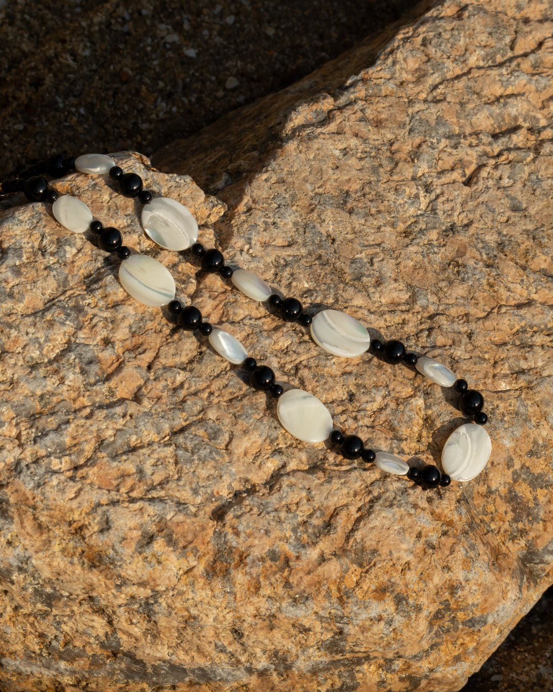 Mother of pearl and onyx necklace, elegantly crafted with white and black beads, showcasing a Sonata Moonlit design, set against a rocky backdrop.