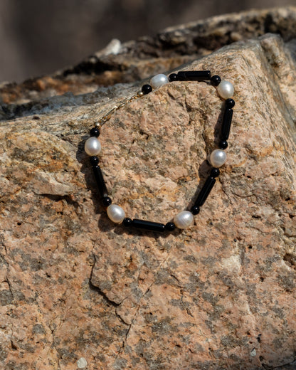 Starry Bracelet onyx: Black onyx and freshwater pearl bracelet, elegantly displaying its vibrant materials against a contrasting stone wall background, serving as a sophisticated accessory for everyday wear. 