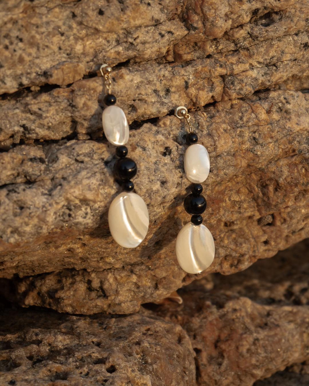 Moonlit Earrings: Onyx earrings, elegantly crafted with lustrous Mother of Pearl stones and sleek black onyx accents, hanging on natural rock, showcasing its owners taste. Perfect for evening wear. 