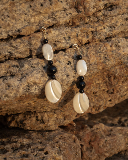 Moonlit Earrings: Onyx earrings, elegantly crafted with lustrous Mother of Pearl stones and sleek black onyx accents, hanging on natural rock, showcasing its owners taste. Perfect for evening wear. 