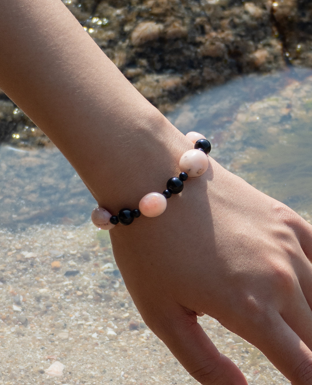 Sonata Blush Bracelet: A delicate piece of jewelry, handcrafted with pink opal and onyx gemstones. Perfect for everyday wear, its vibrant colors and smooth texture make it a must-have accessory. The bracelet is showcased against a natural backdrop, highlighting its beauty and elegance. 