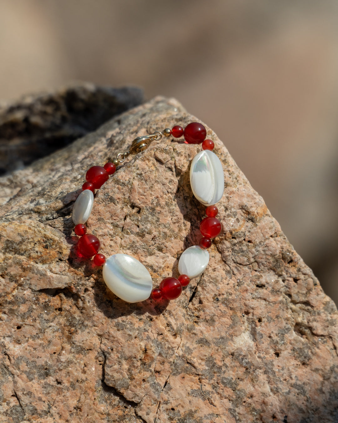 Sonata Moonlit Bracelet, Red Agate and Mother of Pearl (MOP) bracelet, showcasing red agate stone and pearl beads, set against a rock background. 